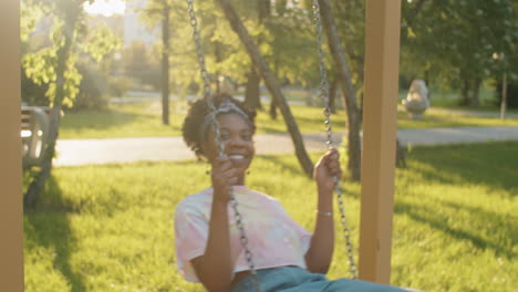 Happy-African-American-Woman-Swinging-on-Swing-in-Park-and-Posing-for-Camera
